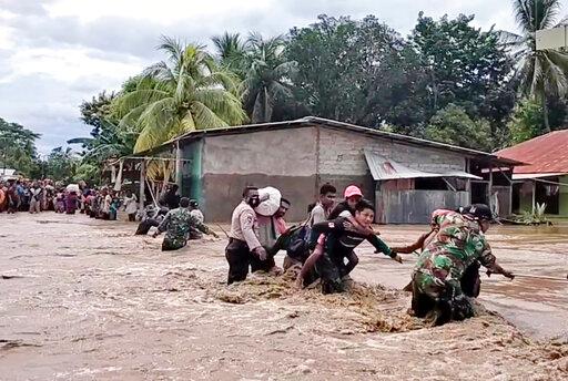 Soldiers and police officers assist residents to cross a flooded road in Malaka Tengah, East Nusa Tenggara province, Indonesia